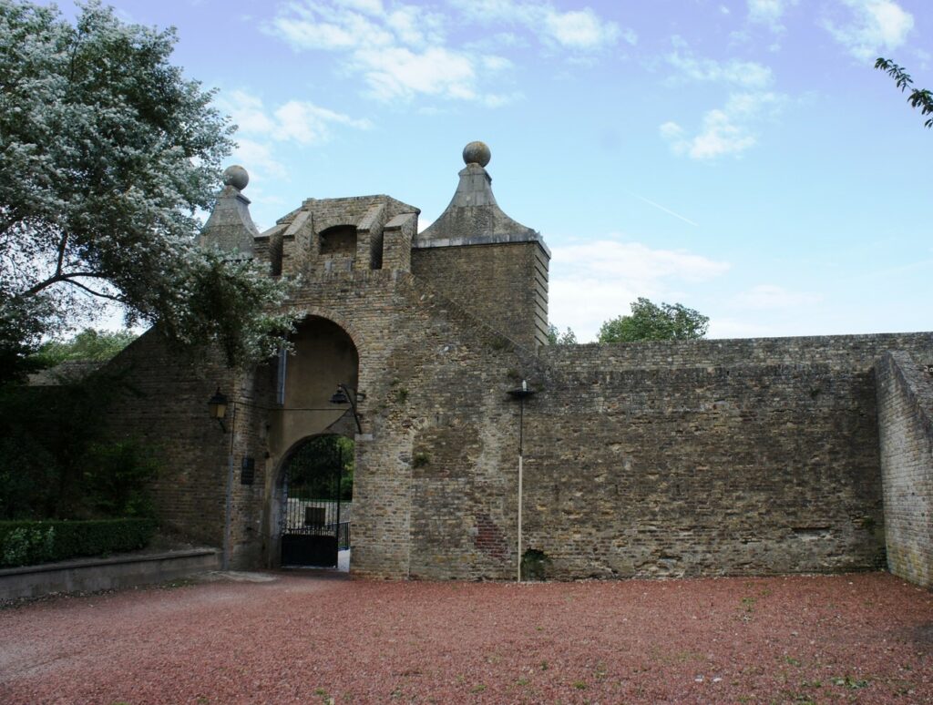 Entrada de la Ciudadela de Calais, una fortificación del siglo XVI rodeada de vegetación y un cielo azul con nubes.