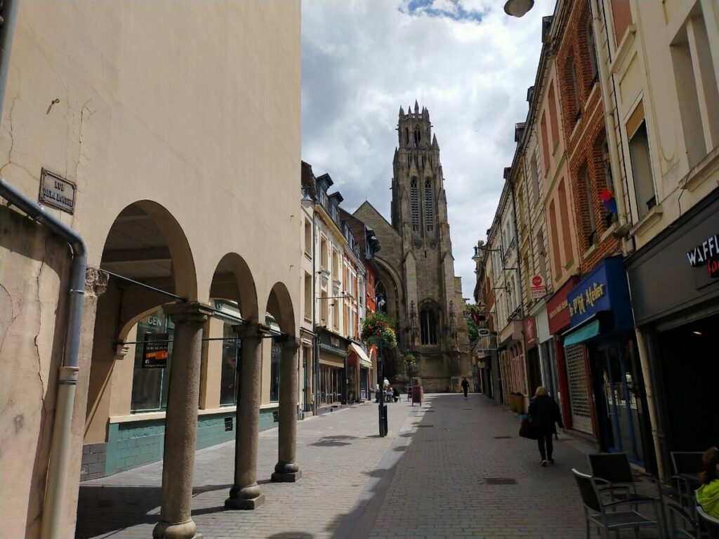 Una calle en Arras, Francia, con edificios de arquitectura clásica, un campanario prominente y una atmósfera tranquila, reflejando el encanto histórico de la ciudad.