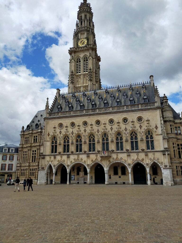 Vista del edificio del campanario en Arras, Francia, con su arquitectura barroca y un cielo nublado.