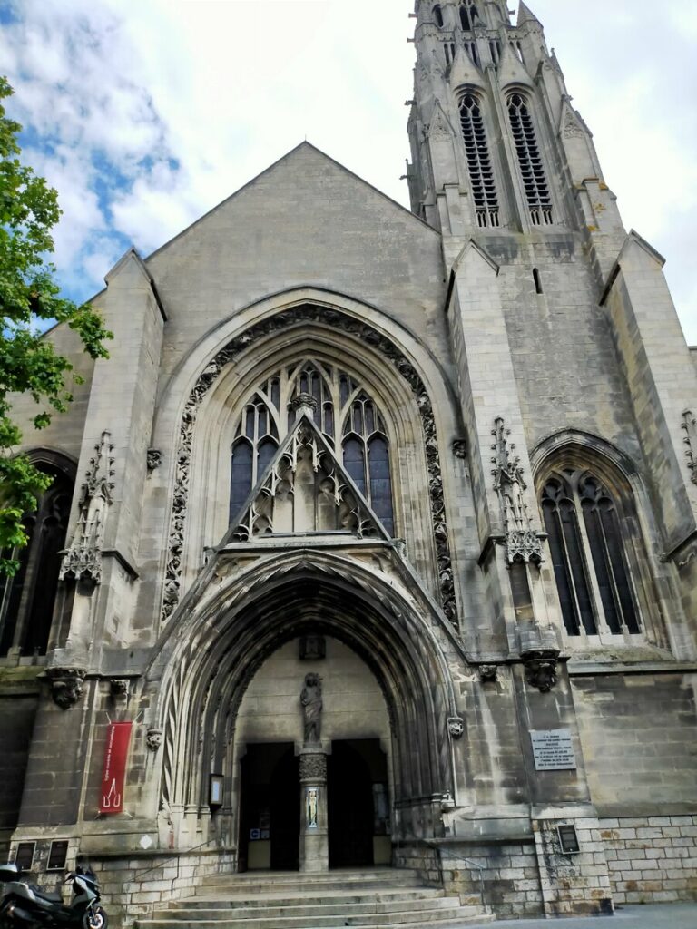 Fachada de una iglesia gótica en Arras, Francia, mostrando su imponente entrada y torre con detalles arquitectónicos elaborados.