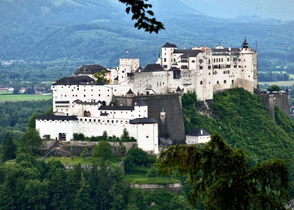 Vista de la fortaleza Hohensalzburg en Salzburgo, Austria, situada sobre una colina verde rodeada de montañas.