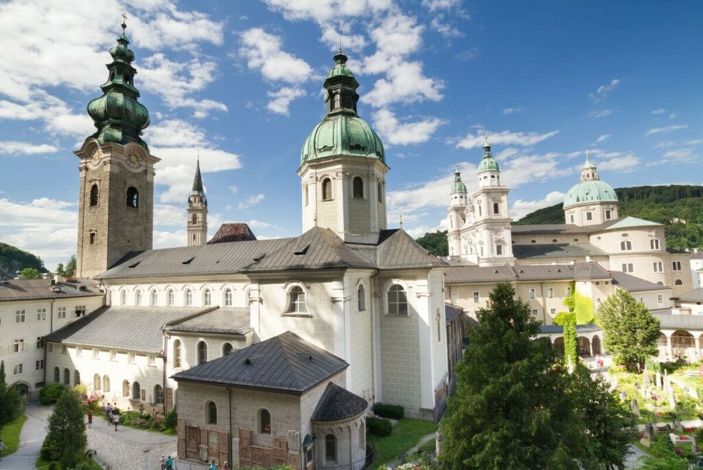 Vista de la arquitectura barroca del Monasterio de San Pedro en Salzburgo, Austria, con torres y cúpulas verdes bajo un cielo azul.